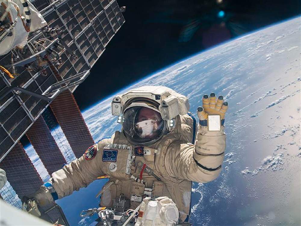 astronauta dando tchau para uma camera no espaço com o planeta terra como plano de fundo