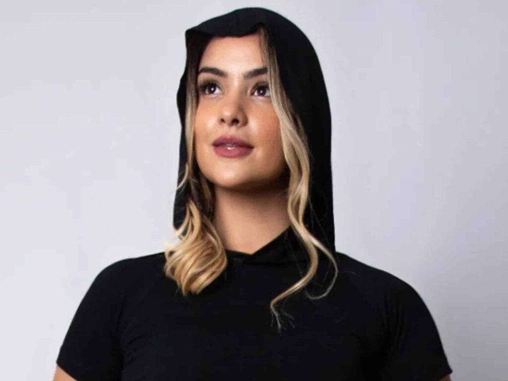 mulher loira olhando para cima usando um casaco preto com capuz em um fundo cinza
