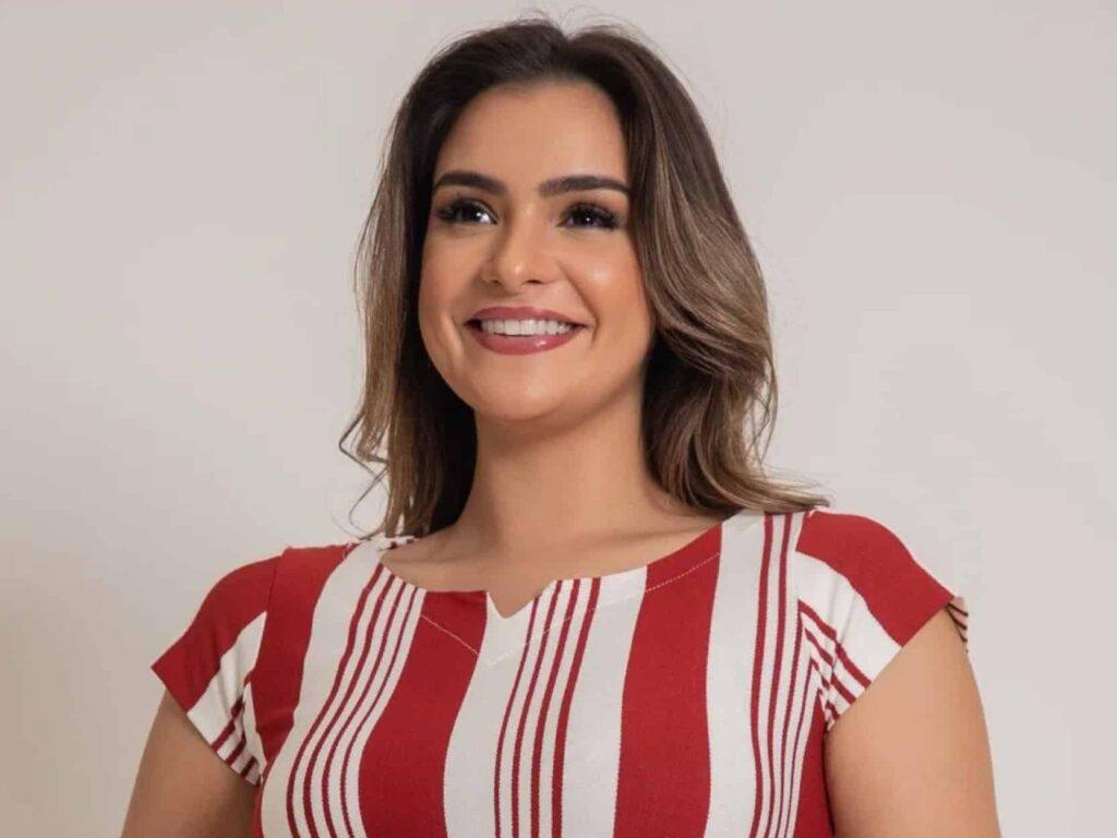 mulher sorrindo para o horizonte em um fundo cinza vestindo uma camiseta vermelha de listras brancas verticais e várias grossuras