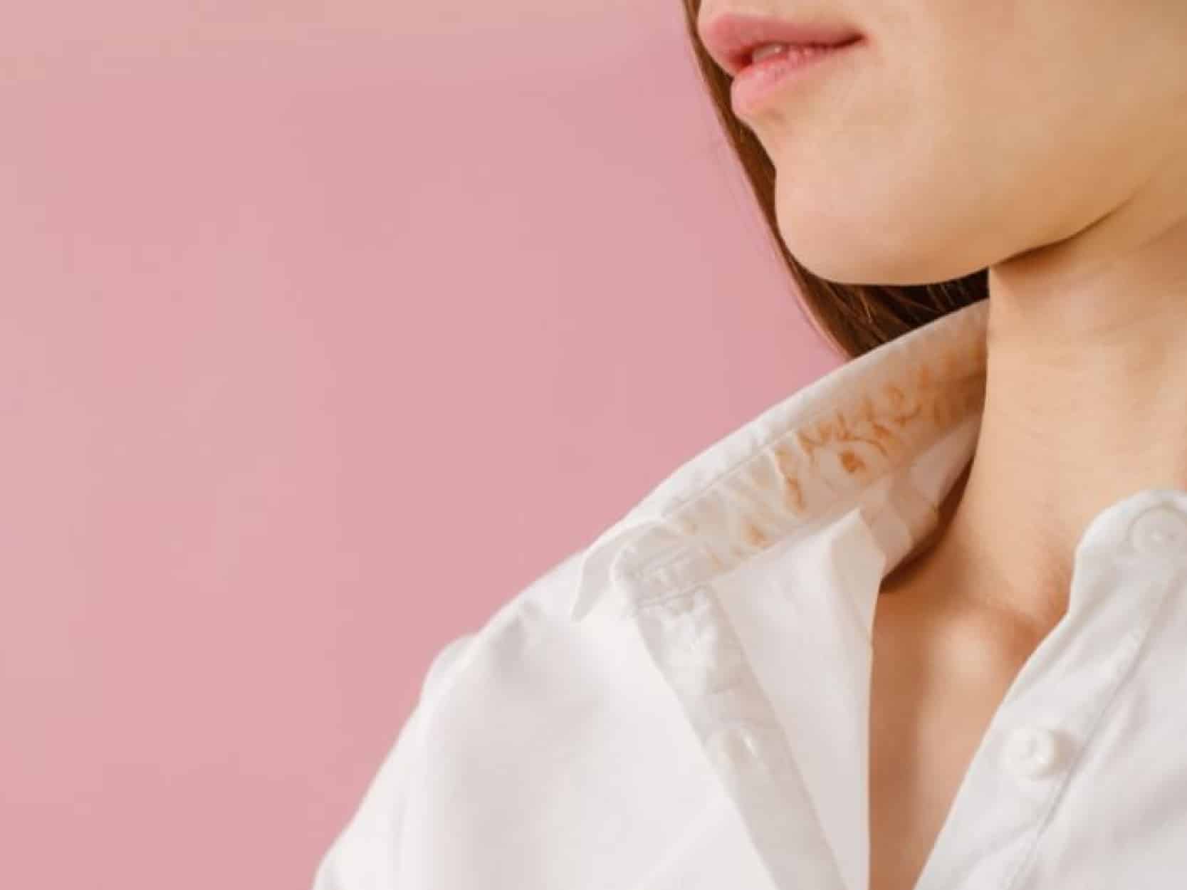 mulher de lado em um fundo rosa usando uma camisa branca manchada de base no colarinho